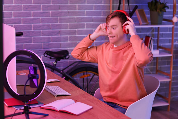 Чоловік студент з навушниками, що транслюються онлайн вдома ввечері - Фото, зображення