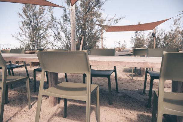 Uma mesa de madeira com cadeiras na areia, em um clube de praia. Decoração elegante, tendas para o sol, plantas. Oásis no deserto. - Foto, Imagem