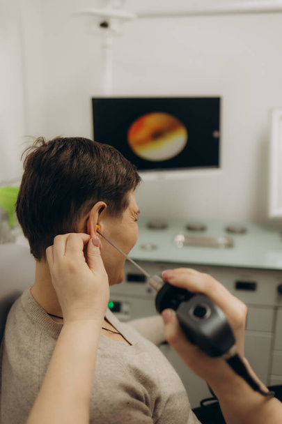 Слухання іспиту для людей похилого віку. Лікар-отоларинголог перевіряє вухо зрілої жінки за допомогою отоскопа або ауріскопа в медичній клініці - Фото, зображення