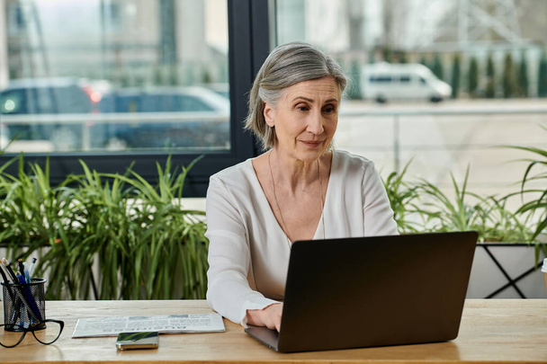 Une femme absorbée dans le travail sur son ordinateur portable à une table. - Photo, image