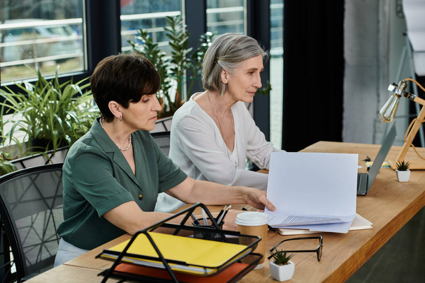 Dos mujeres absortas en el trabajo en un ordenador portátil en una mesa. - Foto, imagen