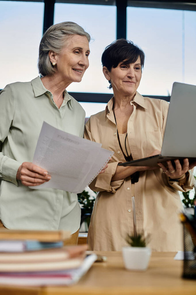 Két nő dolgozik egy laptopon egy irodai környezetben.. - Fotó, kép