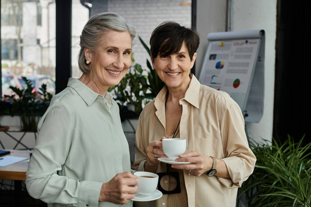 Zwei elegante Frauen, die Tassen in der Hand halten und einen Moment miteinander genießen. - Foto, Bild