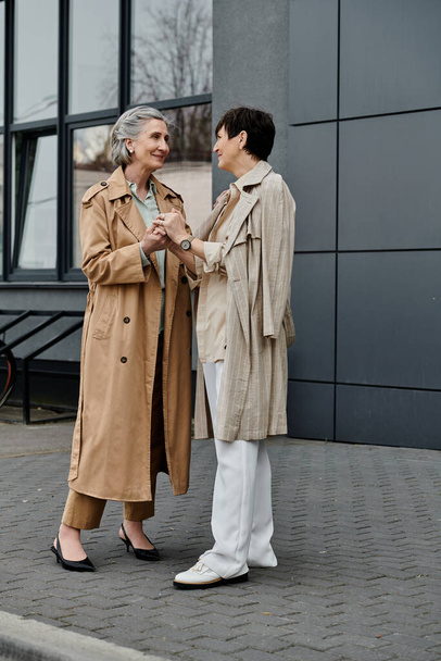 Mature lesbian couple enjoying a stroll in front of a modern building. - Photo, Image