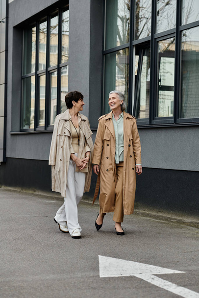 Két érett és gyönyörű nő kéz a kézben sétál végig a nyüzsgő utcán.. - Fotó, kép