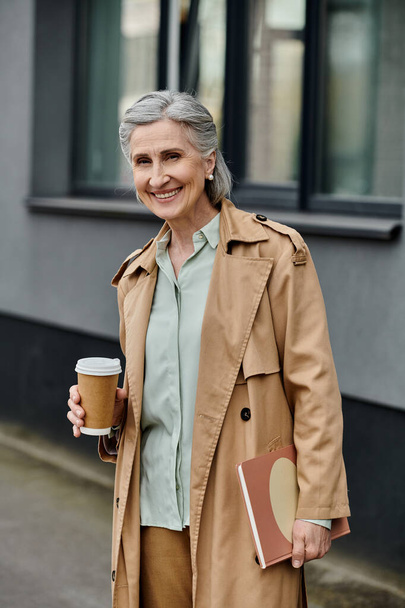 Uma mulher sofisticada em casaco de trincheira desfrutando de uma xícara de café ao ar livre. - Foto, Imagem