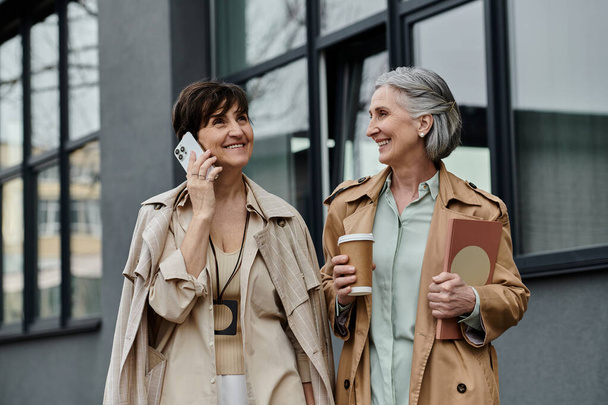 Δύο γυναίκες περπατούν, ασχολούνται με συζήτηση στο κινητό τηλέφωνο. - Φωτογραφία, εικόνα