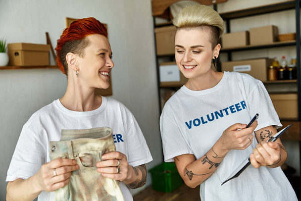 Dwie kobiety, młoda lesbijska para, stoją obok siebie w ochotniczych koszulkach, zjednoczone w pracy charytatywnej. - Zdjęcie, obraz