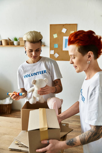 Eine Frau im freiwilligen T-Shirt hält liebevoll einen Teddybär in einem Karton. - Foto, Bild