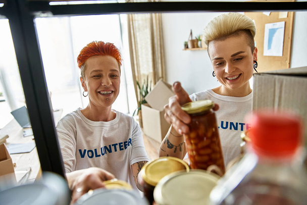 Una pareja de lesbianas con camisetas voluntarias trabajan juntas apasionadamente para marcar la diferencia a través de la caridad. - Foto, Imagen