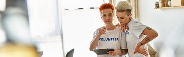 Dvojice žen, které nosí trička s dobrovolníky, stojí v solidaritě a dávají najevo své pouto a závazek k charitativní práci. - Fotografie, Obrázek
