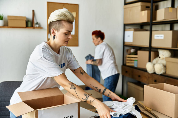 Két fiatal nő önkéntes pólóban kicsomagolja a dobozokat tele tárgyakkal egy szobában, lelkesedéssel dolgoznak együtt.. - Fotó, kép