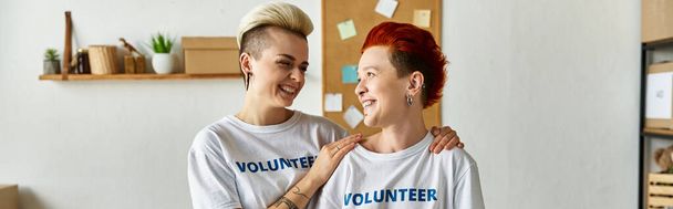 Młoda lesbijska para, ubrana w ochotnicze koszulki, jednocząca się w pracy charytatywnej. - Zdjęcie, obraz