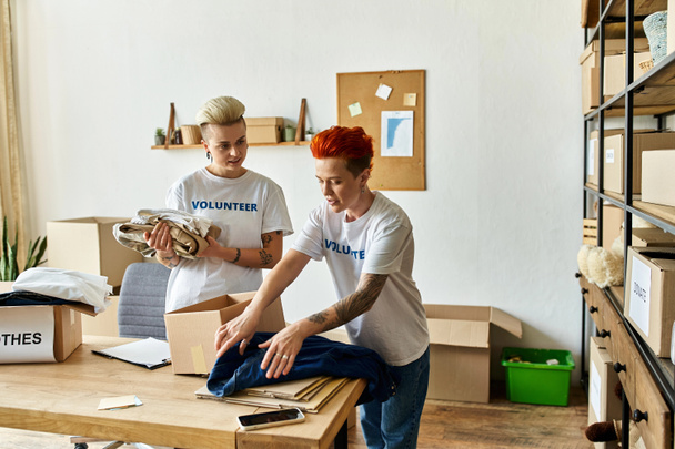Young lesbian couple wearing volunteer t-shirts, working together in a room. - Photo, Image