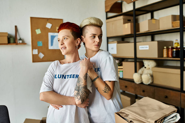 Δύο νεαρές γυναίκες με εθελοντικά μπλουζάκια που στέκονται δίπλα-δίπλα, ενσαρκώνοντας την ενότητα και το σκοπό στο φιλανθρωπικό τους έργο. - Φωτογραφία, εικόνα