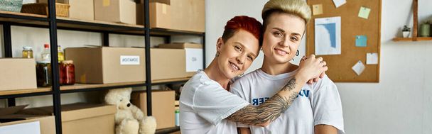 Młoda para lesbijek w ochotniczych koszulach przytula się ciepło, okazując miłość i jedność podczas pracy charytatywnej. - Zdjęcie, obraz