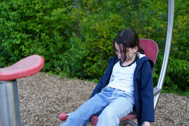 Uma menina de cabelos escuros em óculos está envolvida em um simulador em um playground aberto - Foto, Imagem