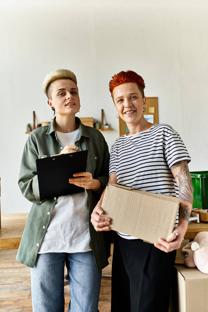 Молодая лесбийская пара стоит бок о бок, держа коробки с пожертвованиями на благотворительность. - Фото, изображение