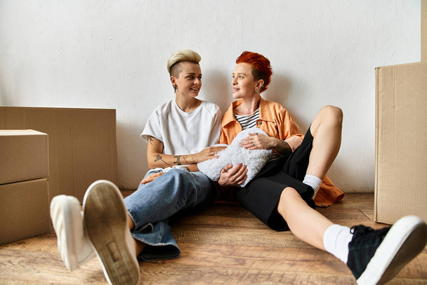 ein junges lesbisches Paar, das in einem Freiwilligenzentrum in der Nähe von Boxen auf dem Boden sitzt und an wohltätigen Projekten arbeitet. - Foto, Bild