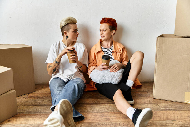 Genç lezbiyen bir çift, kutuların yanında oturmuş, gülümsüyor ve gönüllü bir merkezde birbirlerine eşlik ederek eğleniyorlar.. - Fotoğraf, Görsel