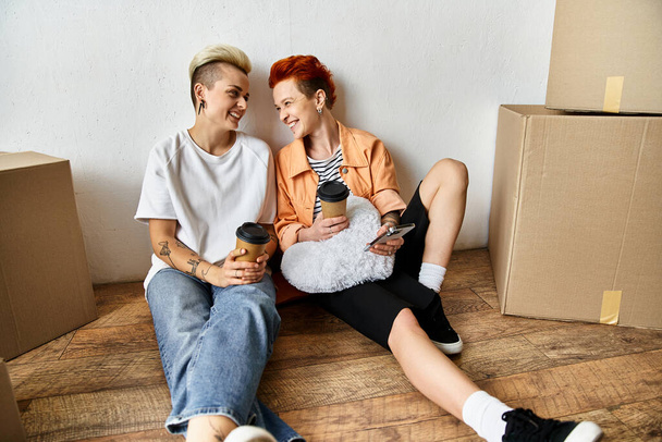 Una joven pareja de lesbianas sentadas en el suelo juntas en un centro de voluntarios rodeado de cajas de donaciones de caridad. - Foto, imagen