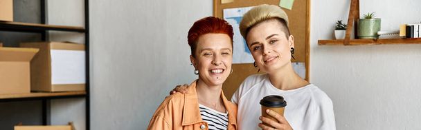 Młoda para lesbijek zjednoczona w centrum wolontariatu otoczona pudłami, ucieleśniająca jedność i wsparcie. - Zdjęcie, obraz