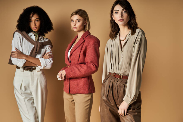 Tre giovani, donne multiculturali in elegante abbigliamento stand uniti su uno sfondo beige, simbolo di amicizia e diversità. - Foto, immagini