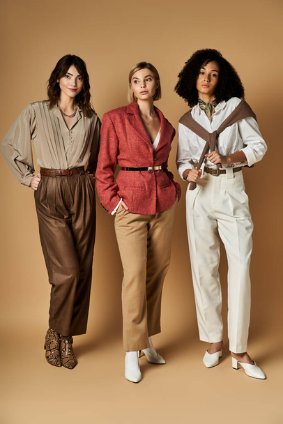 Kolme nuorta, kaunista, monikulttuurista naista tyylikkäässä puvussa poseeraamassa yhdessä beigellä pohjalla. - Valokuva, kuva