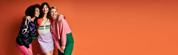 Un groupe diversifié de jeunes, belles femmes en vêtements vibrants se tiennent ensemble sur un fond orange, mettant en valeur l'amitié et la diversité culturelle. - Photo, image