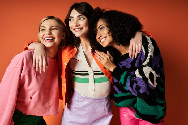 Um grupo de jovens, mulheres bonitas em roupas vibrantes de diferentes culturas que estão juntos em um fundo laranja. - Foto, Imagem