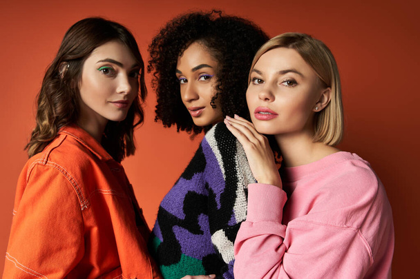 Tre giovani donne multiculturali stanno con stile davanti a un vivace sfondo rosso, mettendo in mostra la diversità nella moda e nella cultura.. - Foto, immagini