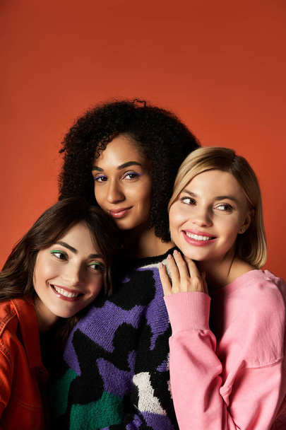 Három különböző kultúrájú fiatal, stílusos nő pózol együtt egy feltűnő narancssárga háttérben.. - Fotó, kép