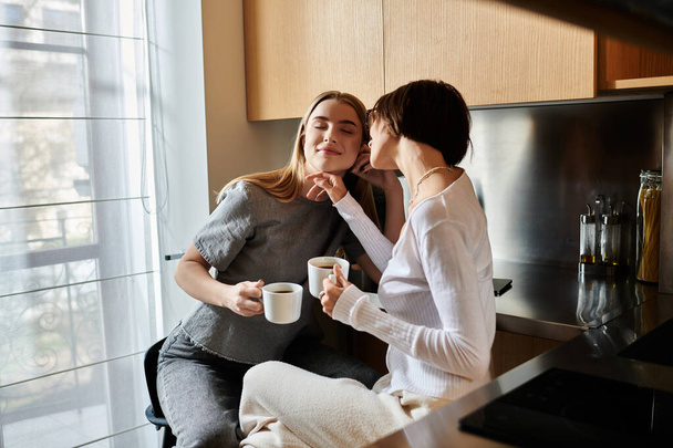 Δύο γυναίκες σε μια κουζίνα ξενοδοχείου, πίνοντας καφέ μαζί, επιδεικνύοντας αγάπη και ενότητα. - Φωτογραφία, εικόνα