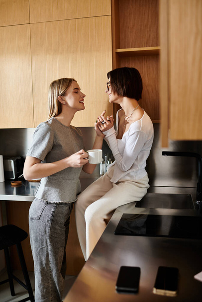 Dos mujeres jóvenes comparten un momento acogedor en la cocina de un hotel, saboreando su café juntas. - Foto, imagen