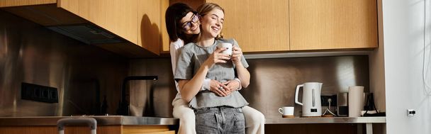 Молодая лесбийская пара стоит на кухне отеля, наслаждаясь кофе вместе. - Фото, изображение