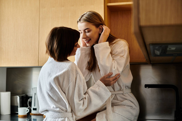 Δύο νεαρές γυναίκες, ένα ζευγάρι λεσβιών, στέκονται μαζί σε μια κομψή κουζίνα, επιδεικνύοντας αγάπη και συντροφικότητα.. - Φωτογραφία, εικόνα