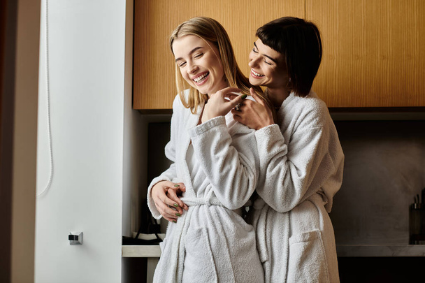 Ein junges lesbisches Paar steht in Bademänteln in einem Hotelzimmer zusammen und strahlt Ruhe und Intimität aus. - Foto, Bild