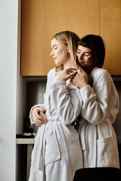 Un jeune couple lesbien en peignoir, debout côte à côte dans une chambre d'hôtel, exsudant sérénité et amour. - Photo, image