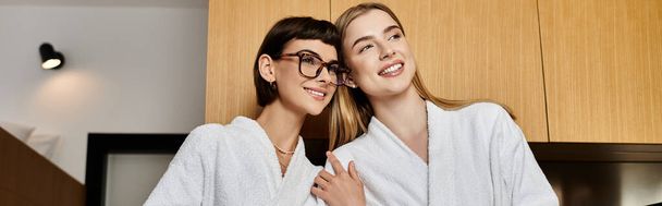 A tranquil scene of a young lesbian couple in bath robes embracing in a cozy hotel room. - Photo, Image