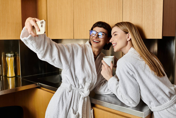 Nuori lesbo pari kylpytakissa ottaa selfien ylellisessä hotellin kylpyhuoneessa. - Valokuva, kuva
