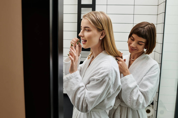 Zwei junge Frauen, ein lesbisches Paar, stehen in einem Hotelbadezimmer vor einem Spiegel - Foto, Bild