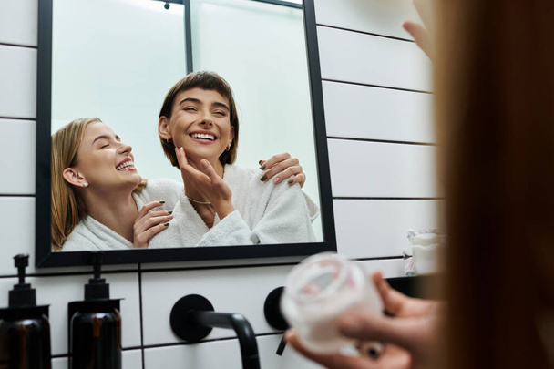 Молоді жінки в лазні стоять перед дзеркалом, застосовуючи крем у ванній кімнаті готелю. - Фото, зображення