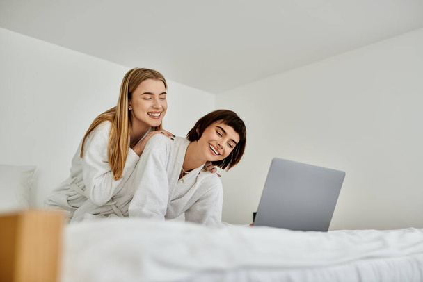 Una coppia lesbica in accappatoi, rilassarsi in cima a un letto in una camera d'albergo, condividere un momento accogliente e intimo. - Foto, immagini