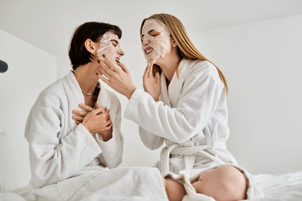 Una hermosa pareja lesbiana con túnicas blancas sentada tranquilamente en una cama dentro de una habitación de hotel. - Foto, Imagen