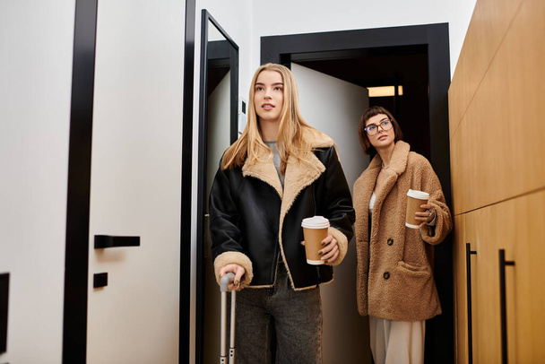 Nuori lesbo pari matkatavarat, tyylikkäästi seisoo yhdessä hotellin käytävällä. - Valokuva, kuva
