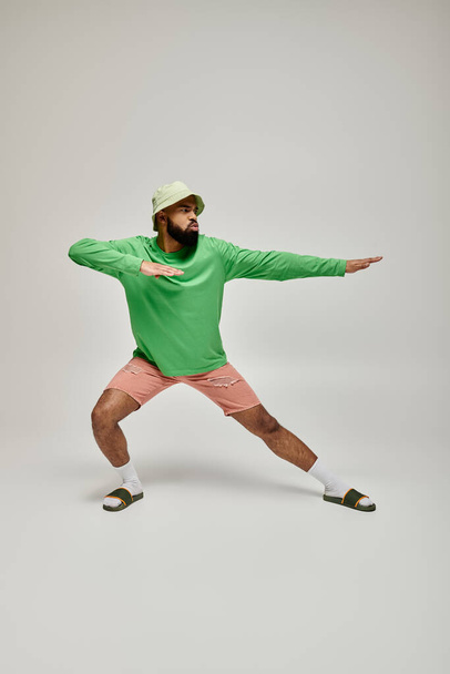 ファッショナブルな緑のシャツと活気に満ちた背景にポーズするピンクのショートパンツでハンサムなアフリカ系アメリカ人. - 写真・画像