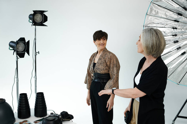Lesbisches Paar mittleren Alters in einem Studio; eine Frau steht vor der Kamera, die andere fängt ihre Schönheit ein. - Foto, Bild