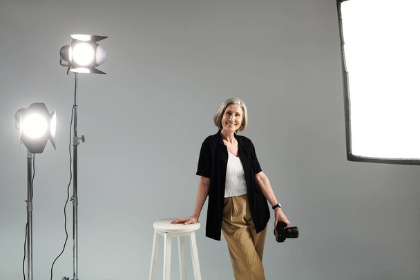 Photographe d'âge moyen avec appareil photo numérique frappant une pose en studio photo - Photo, image