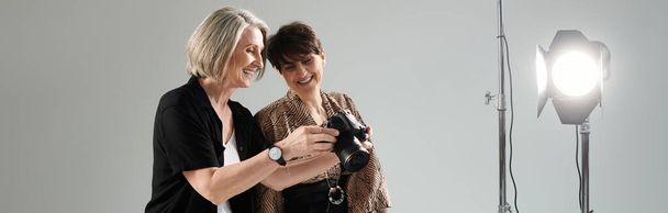 A middle-aged lesbian couple in a photo studio; one is a photographer with a camera, the other is a model. - Photo, Image
