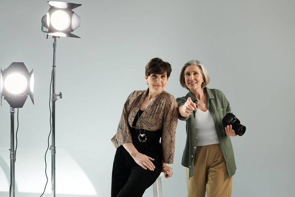 Para lesbijek w średnim wieku w studiu fotograficznym, jedna nagrywa aparatem, druga udaje modelkę. - Zdjęcie, obraz